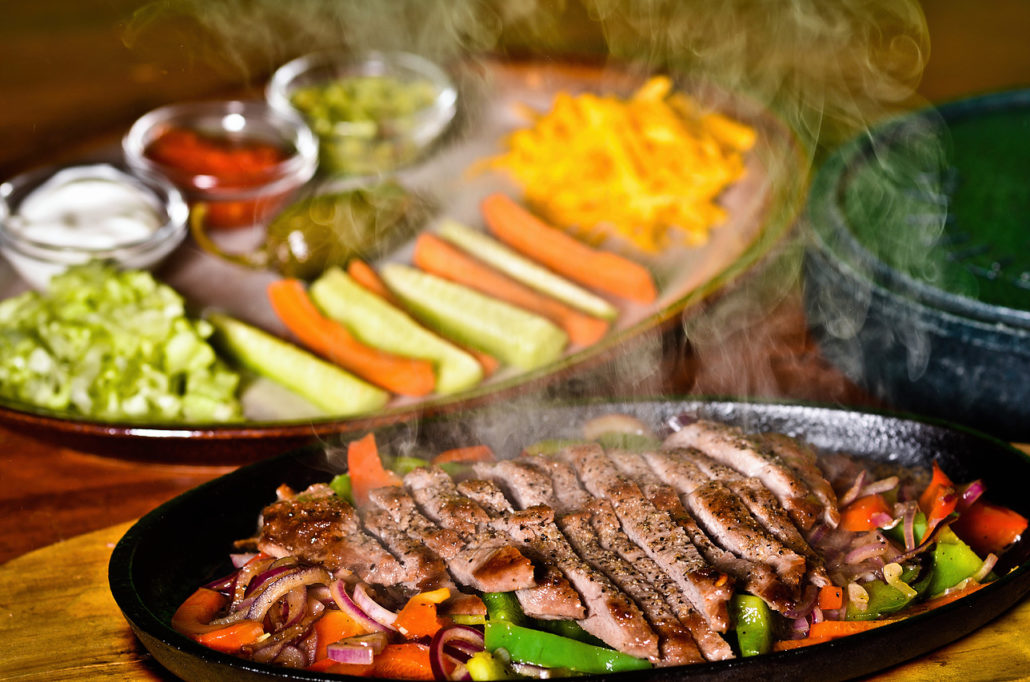 Fajitas na pánvi, vedle talíř s guacamole, salsou a nakládanou zeleninou